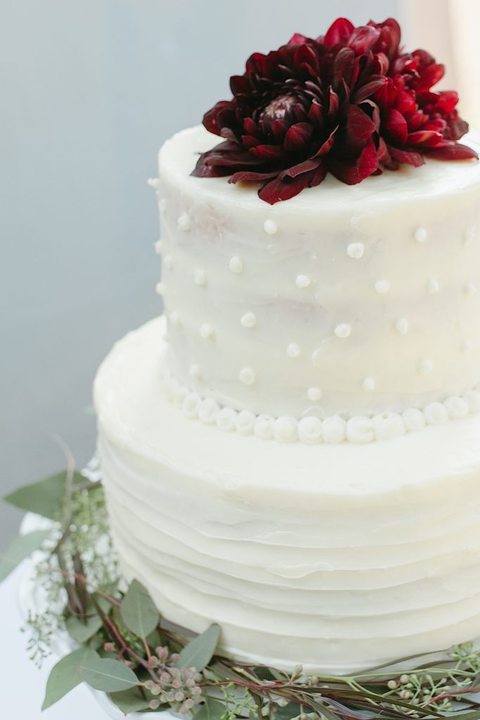 white wedding cake with red dahlia flower on top